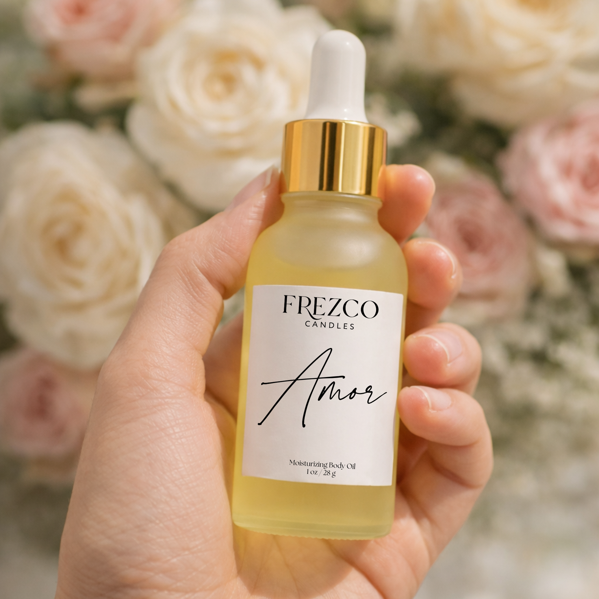 Hand holding a bottle of FREZCO Candles 'Amor' body oil with flowers in the background