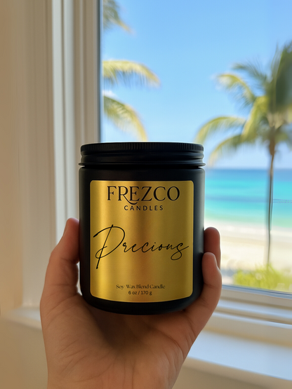 Frezco Candles 'Precious' candle held in front of a window with a beach view