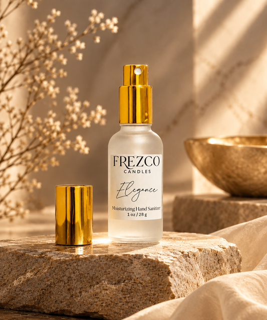 A bottle of Frezco Candle Elegance moisturizing hand sanitizer with a gold pump and a separate gold cap, styled on a stone slab with dried flowers and a bowl in a warm, sunlit setting.